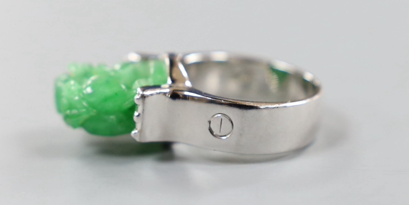 A 585 white metal and jadeite ring, carved with a lion dog, size O, gross weight 11.1 grams.